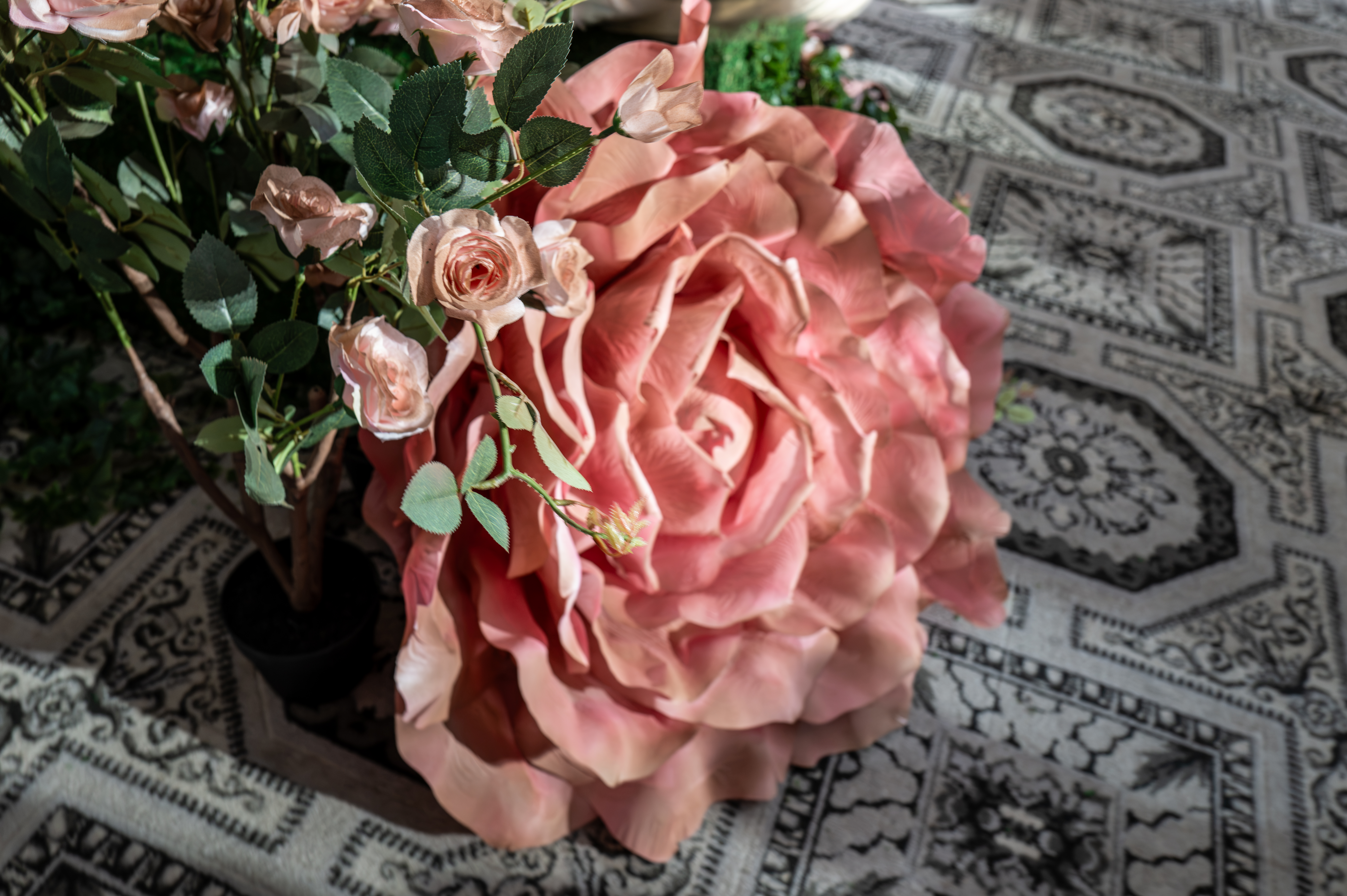 An oversized pink rose centerpiece staged on a patterned rug as part of the set design at Alice + Olivia's Wonderland presentation.