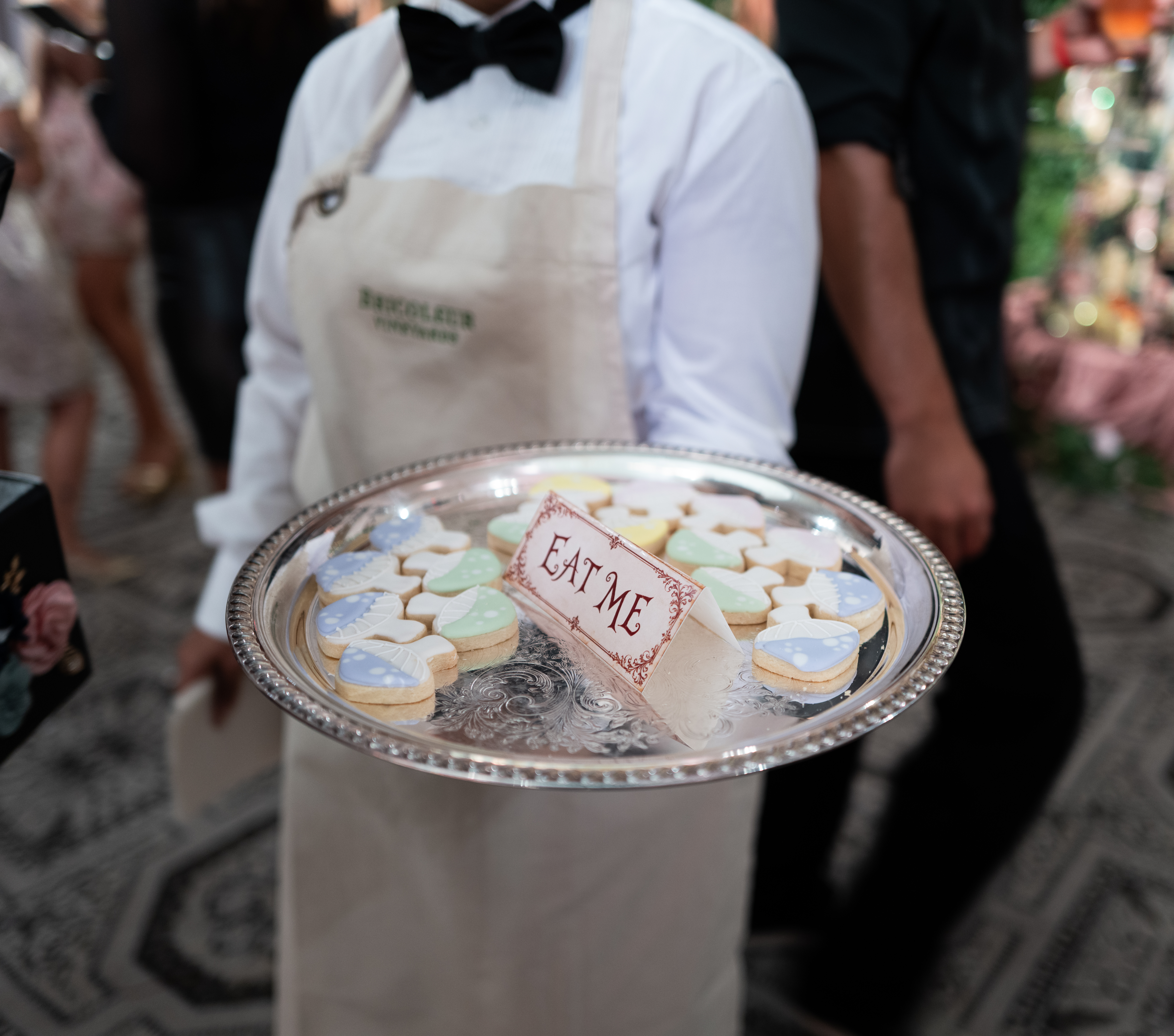 A silver tray of pastel-iced 'Eat Me' cookies, referencing Alice in Wonderland, served to guests at Alice + Olivia's Spring 2027 presentation.