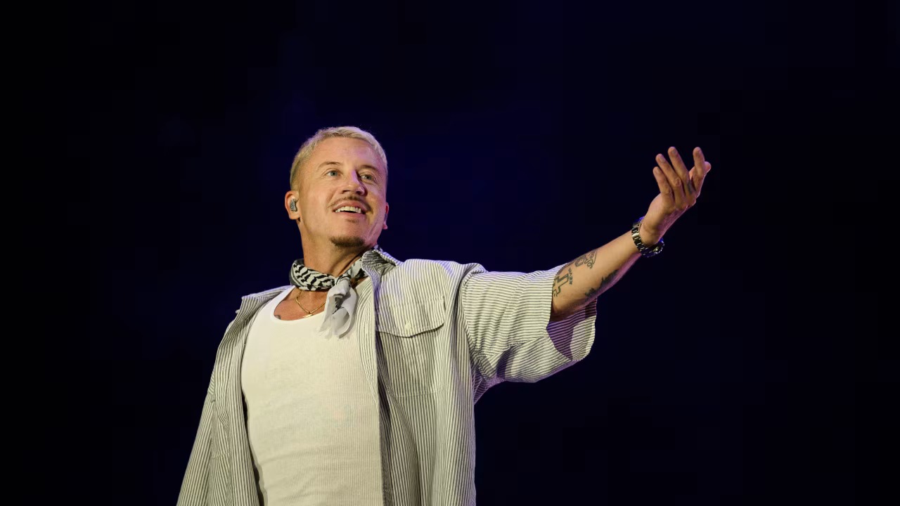Macklemore performs on stage wearing a keffiyeh scarf.