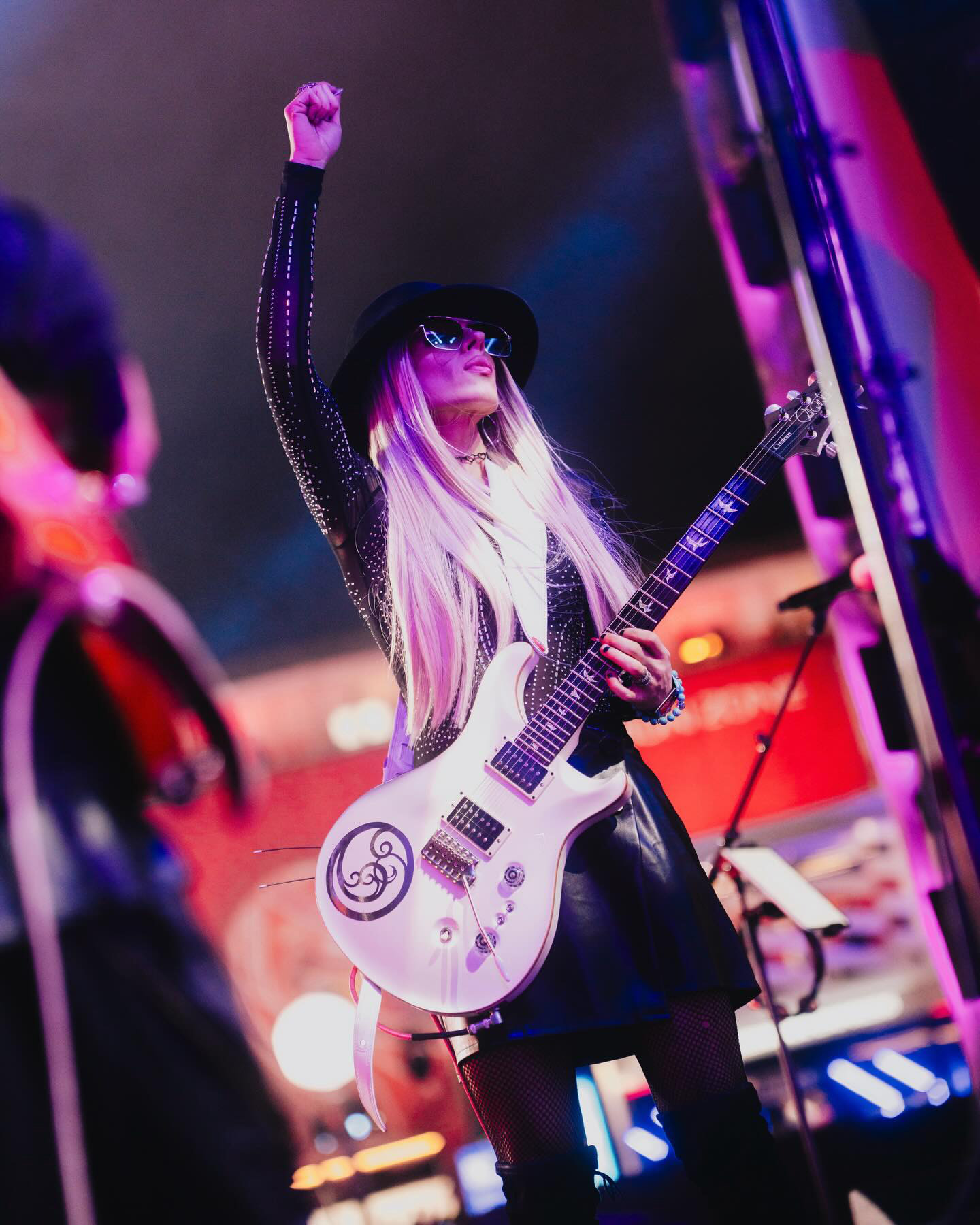 Orianthi raising her fist on stage with her white PRS guitar